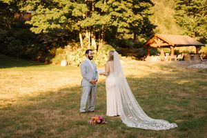 Outdoor wedding ceremony in a sunlit meadow surrounded by trees during golden hour.