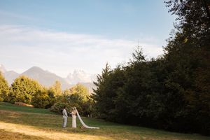 Mountain peaks rise above a green meadow with a decorative metal arch structure in autumn light.