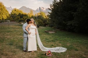 Elegant wedding couple embraces outdoors while the bride's lace veil flows gracefully in the breeze.