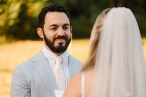 A couple in light-colored wedding attire poses together during their outdoor summer ceremony.