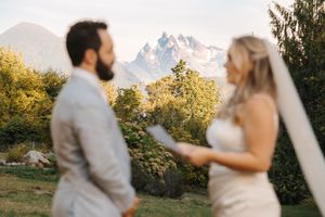 A couple in wedding attire embraces in front of majestic mountain peaks during a golden sunset.