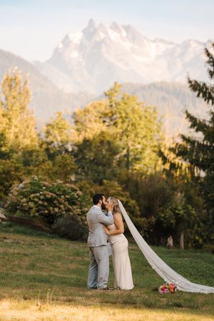 A couple embraces in a romantic mountain meadow at sunset with fall foliage and mountains in the background.
