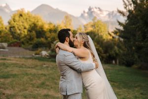 A couple shares a romantic embrace during their outdoor wedding with majestic mountains and autumn trees in the background.