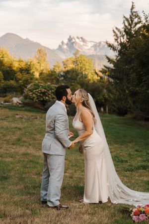 Beautiful outdoor wedding ceremony in a grassy field with mountain peaks and warm sunset light in the background.