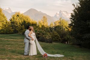Couple in wedding attire embrace lovingly in scenic mountain meadow during golden hour.