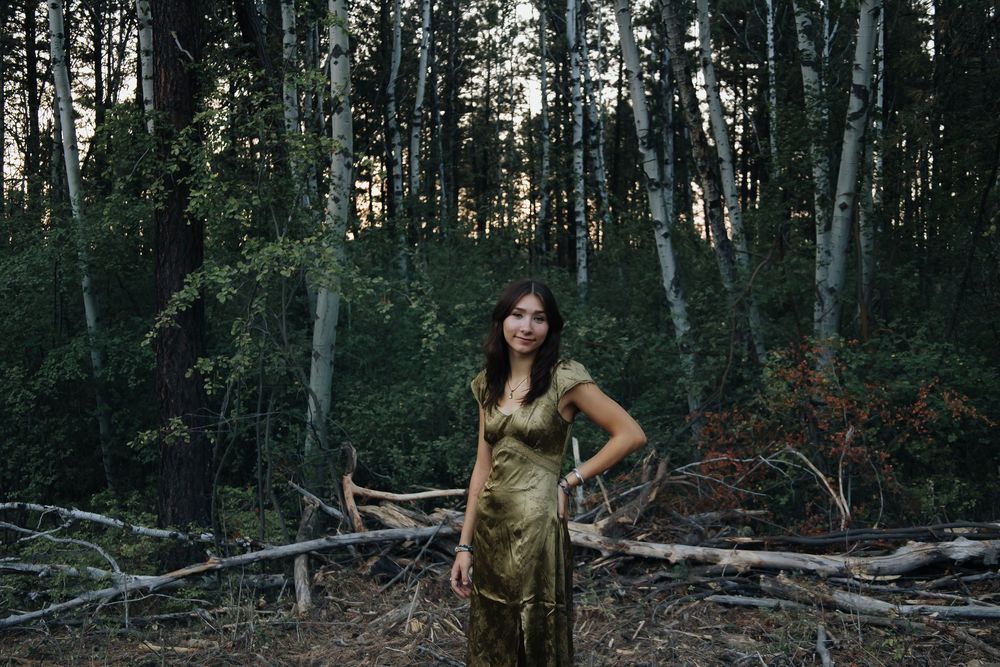A forest photoshoot featuring a gold dress against dark woods and fallen trees.