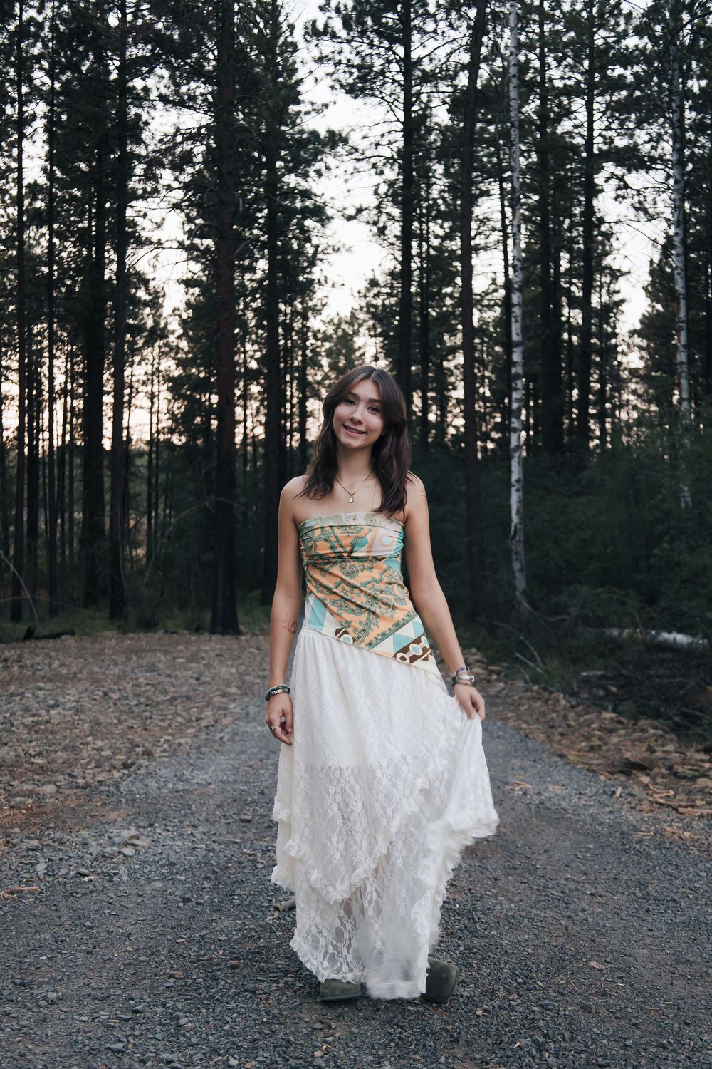 Person in white lace dress twirling on a forest path at sunset.