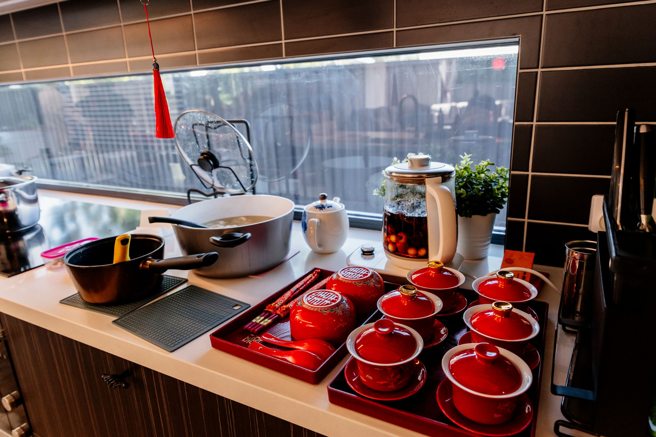 Red teacups and bowls arranged on a wooden counter with a window view and small indoor plant.
