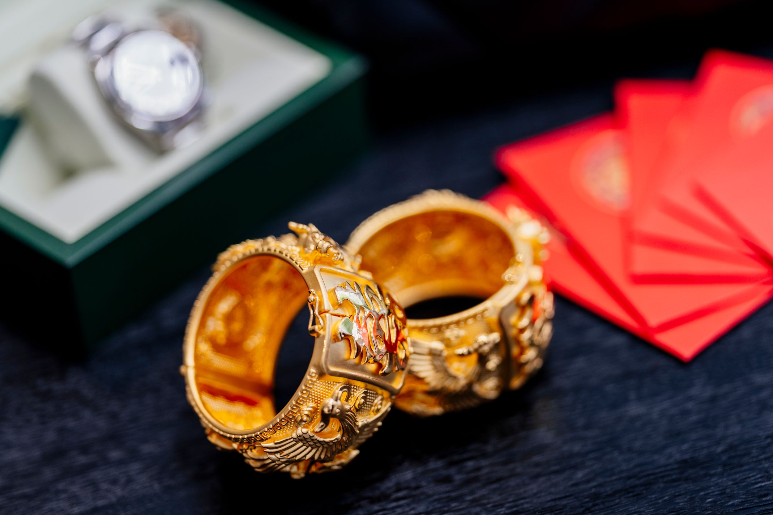 Ornate gold wedding rings with intricate designs displayed on dark background with red elements.