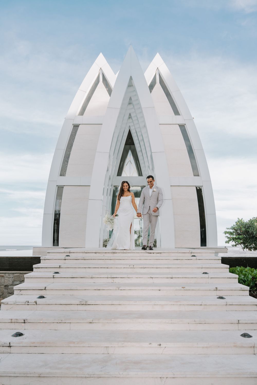 A modern white architectural monument with steps leading to a triangular arch design against a cloudy sky.