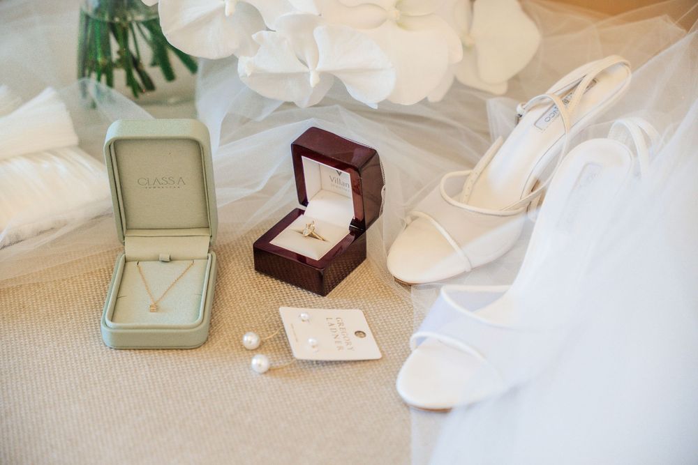 White wedding dress details with delicate lace fabric and silk trim laid out with jewelry boxes and floral accessories.
