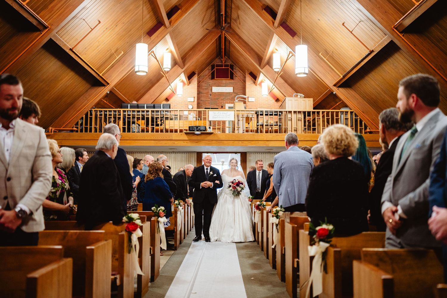 Church wedding ceremony takes place in a rustic wooden chapel with exposed beam ceiling and natural lighting.