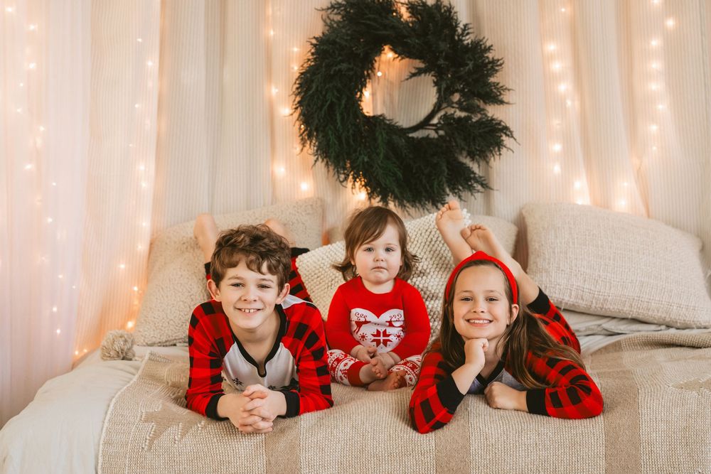 A group wearing matching red and black buffalo plaid outfits poses on a couch with twinkling lights in the background.