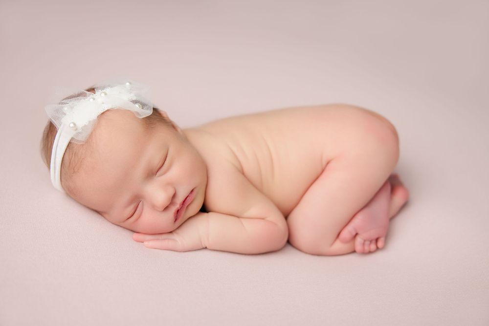 A sleeping newborn baby lies peacefully on soft pink fabric in a minimalist studio portrait setting.