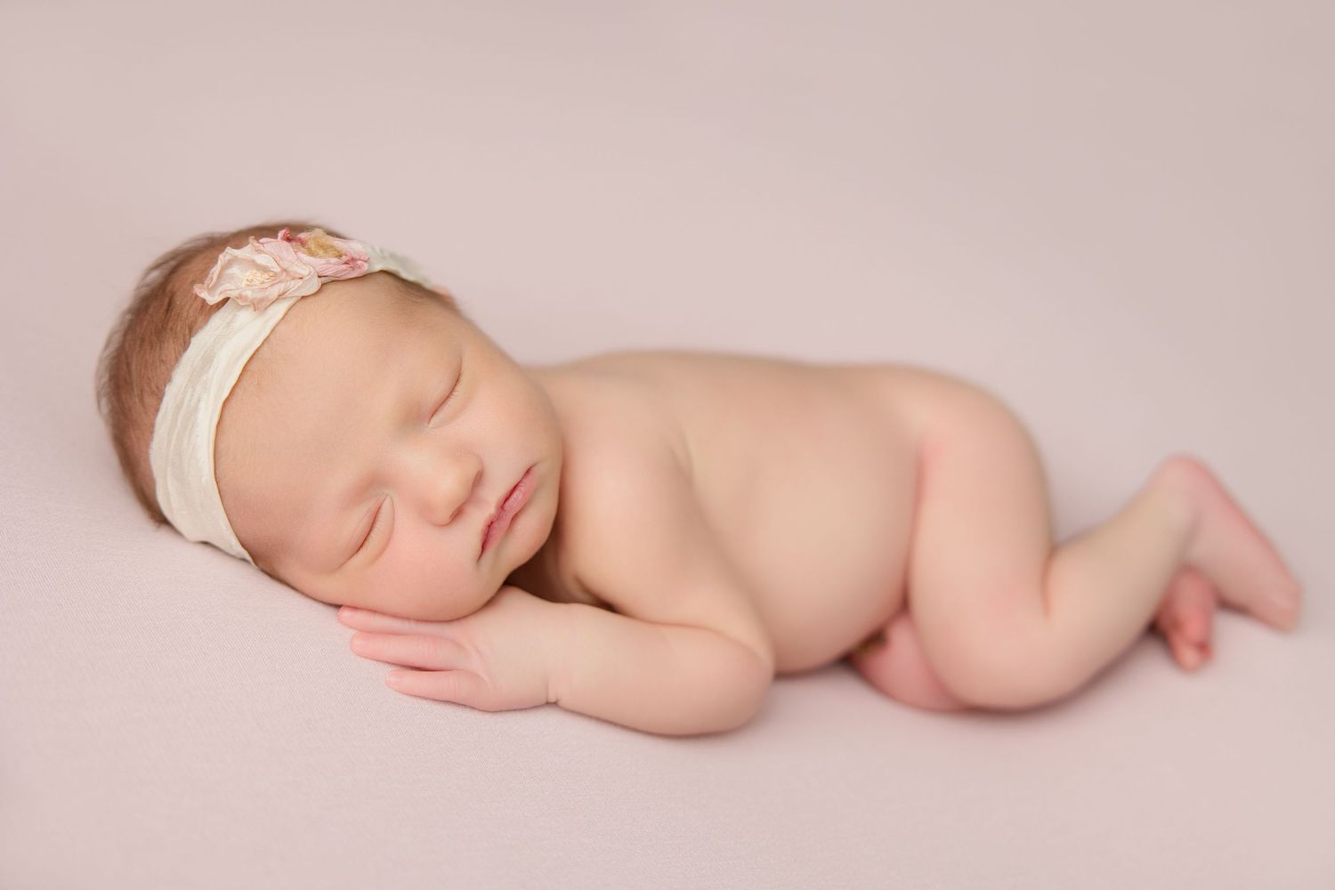Peaceful sleeping newborn baby curled up in soft pink lighting during professional photography session.