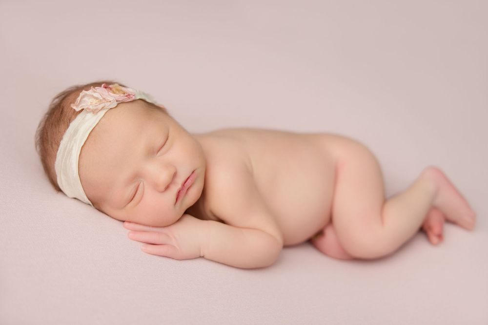 Peaceful sleeping newborn baby curled up in soft pink lighting during professional photography session.