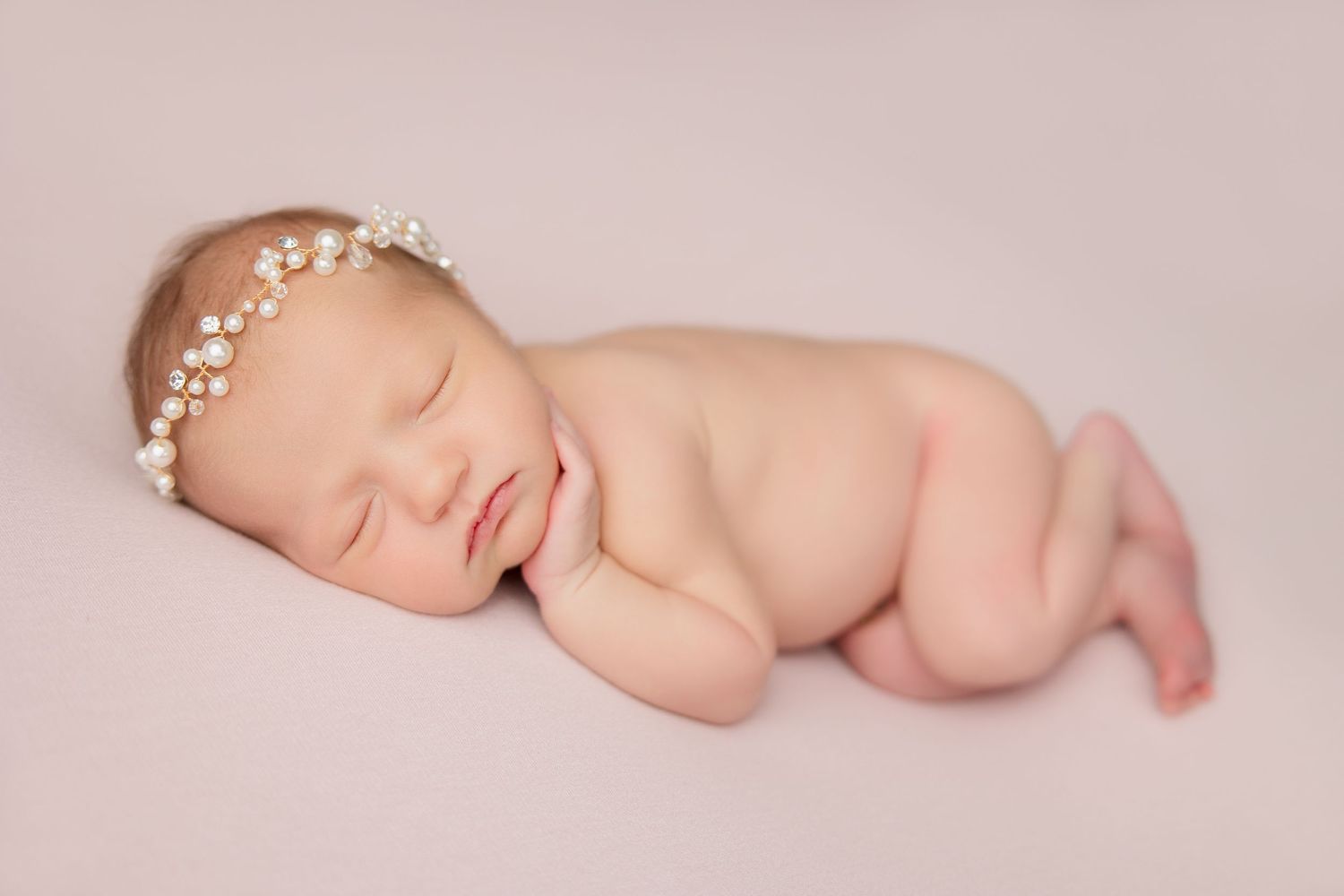 A sleeping newborn baby lies peacefully in natural lighting against a soft pink backdrop.