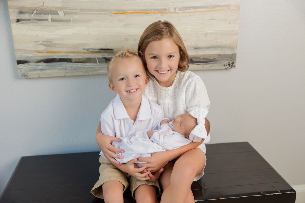 Family photo with children sitting together on a white couch with abstract art on wall behind them.