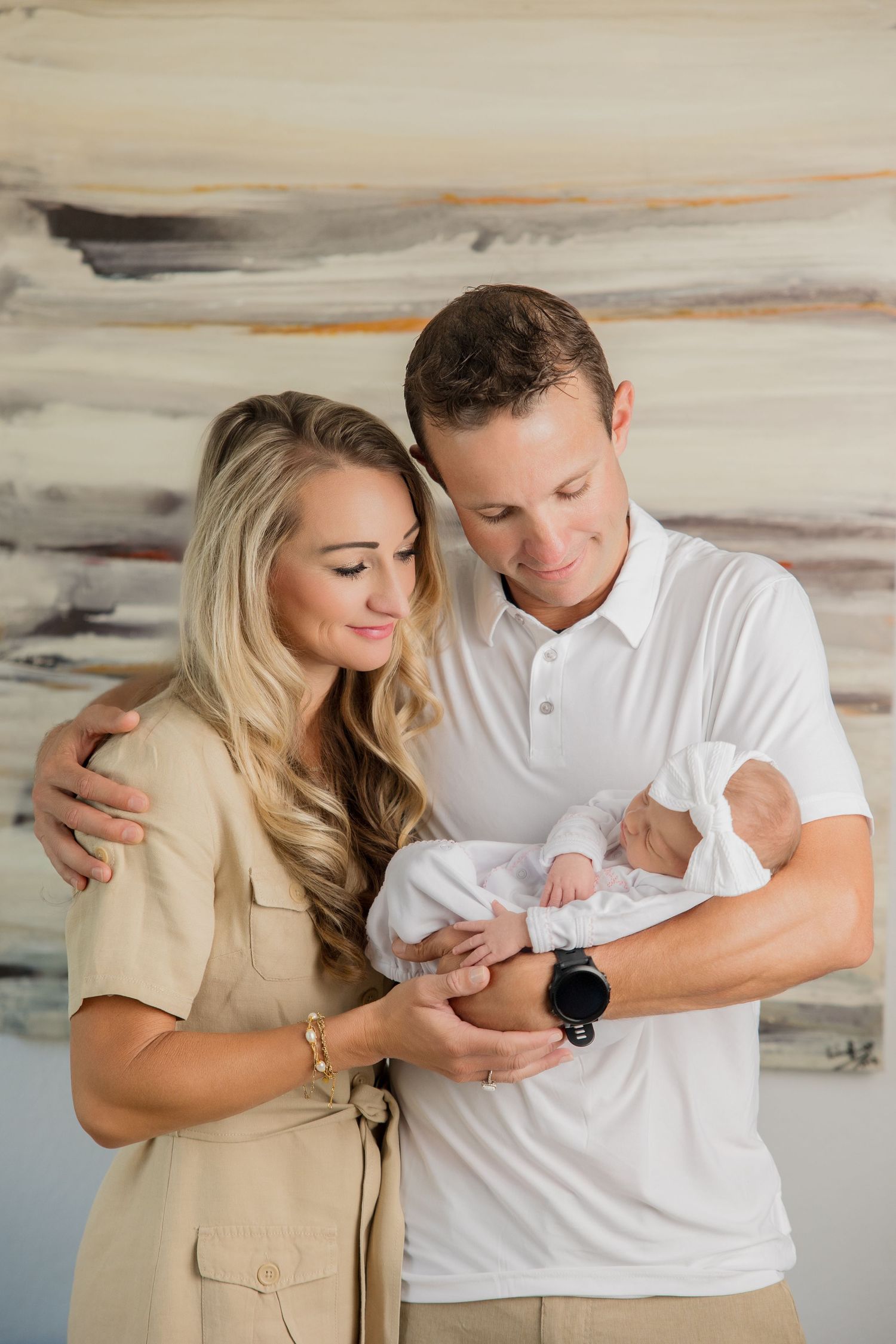 A couple in neutral colored clothing shares tender moments while holding their newborn baby in a minimalist studio setting.