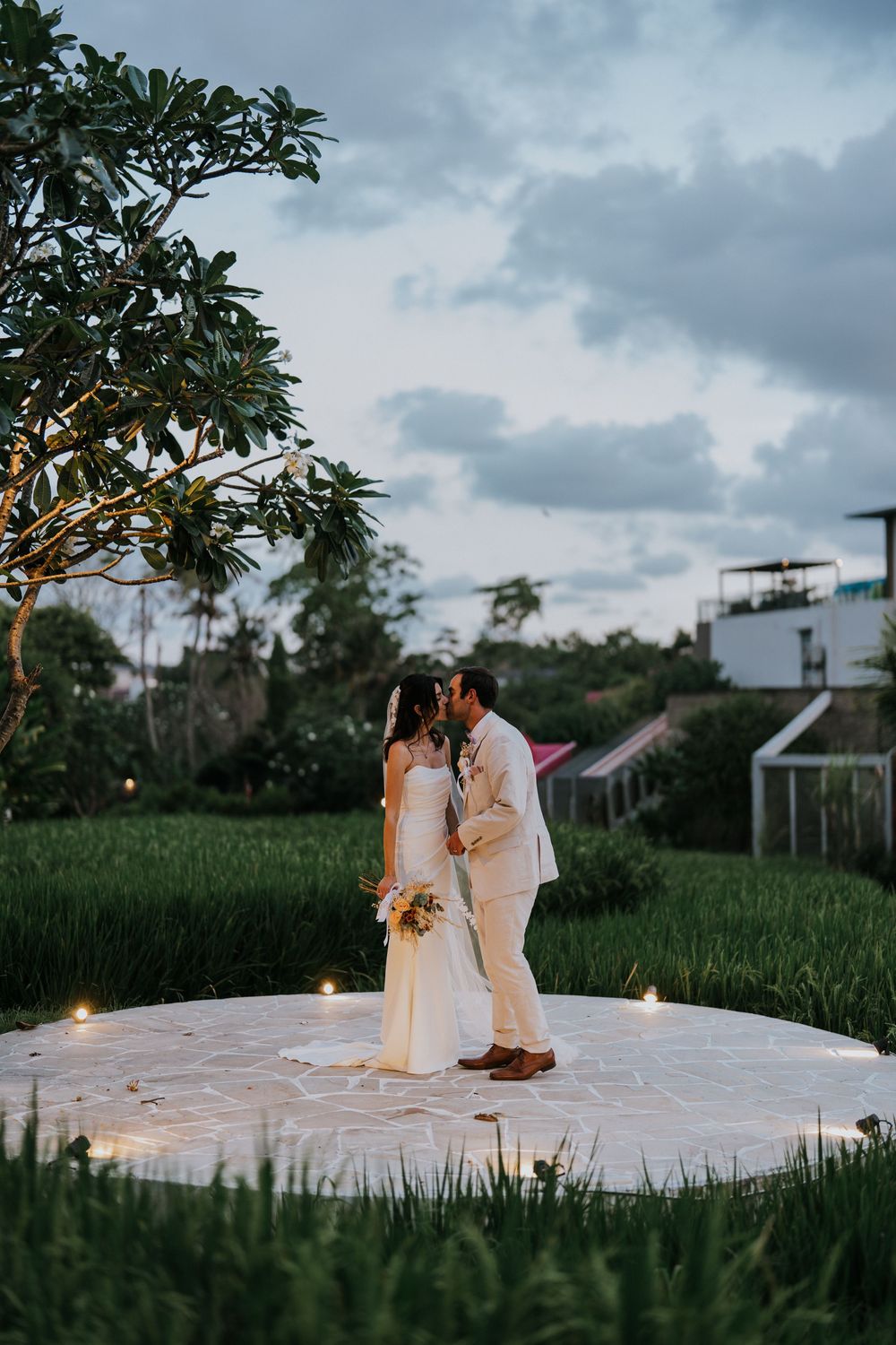 A romantic moment captured on a white platform surrounded by lush green rice fields at sunset.