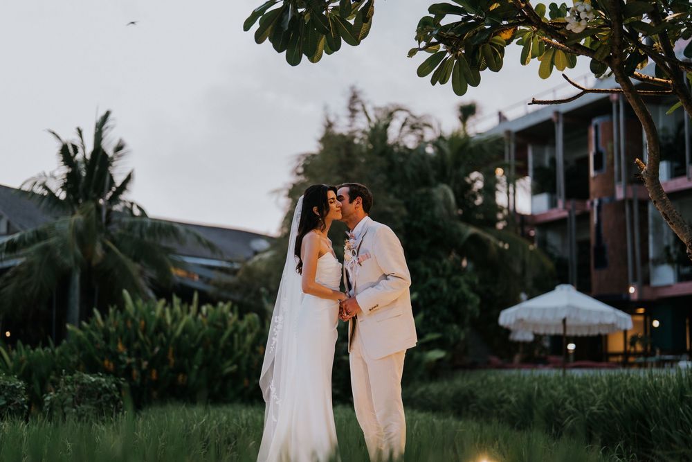 Evening wedding photography with couple walking beneath lush green trees.