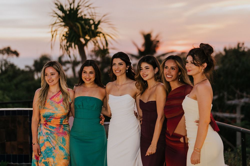 A group wearing colorful dresses poses together at sunset during a special celebration.