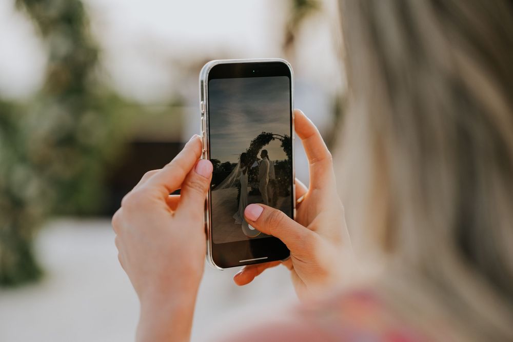 Wedding guests hold up phones to capture a special moment during an outdoor ceremony.