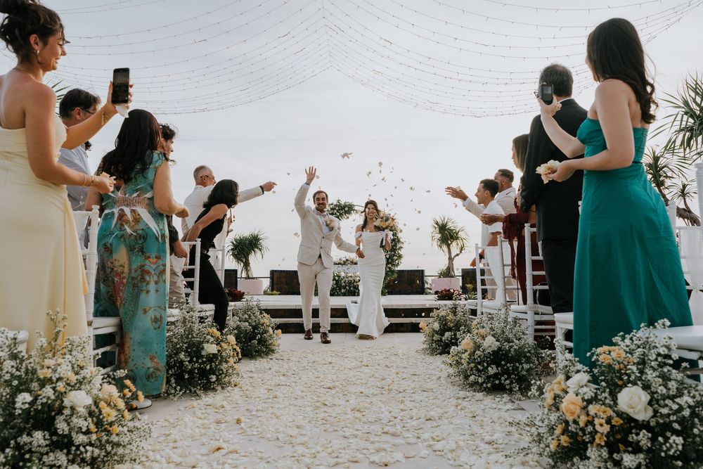 Guests seated in white chairs at an outdoor wedding ceremony with floral decorations.