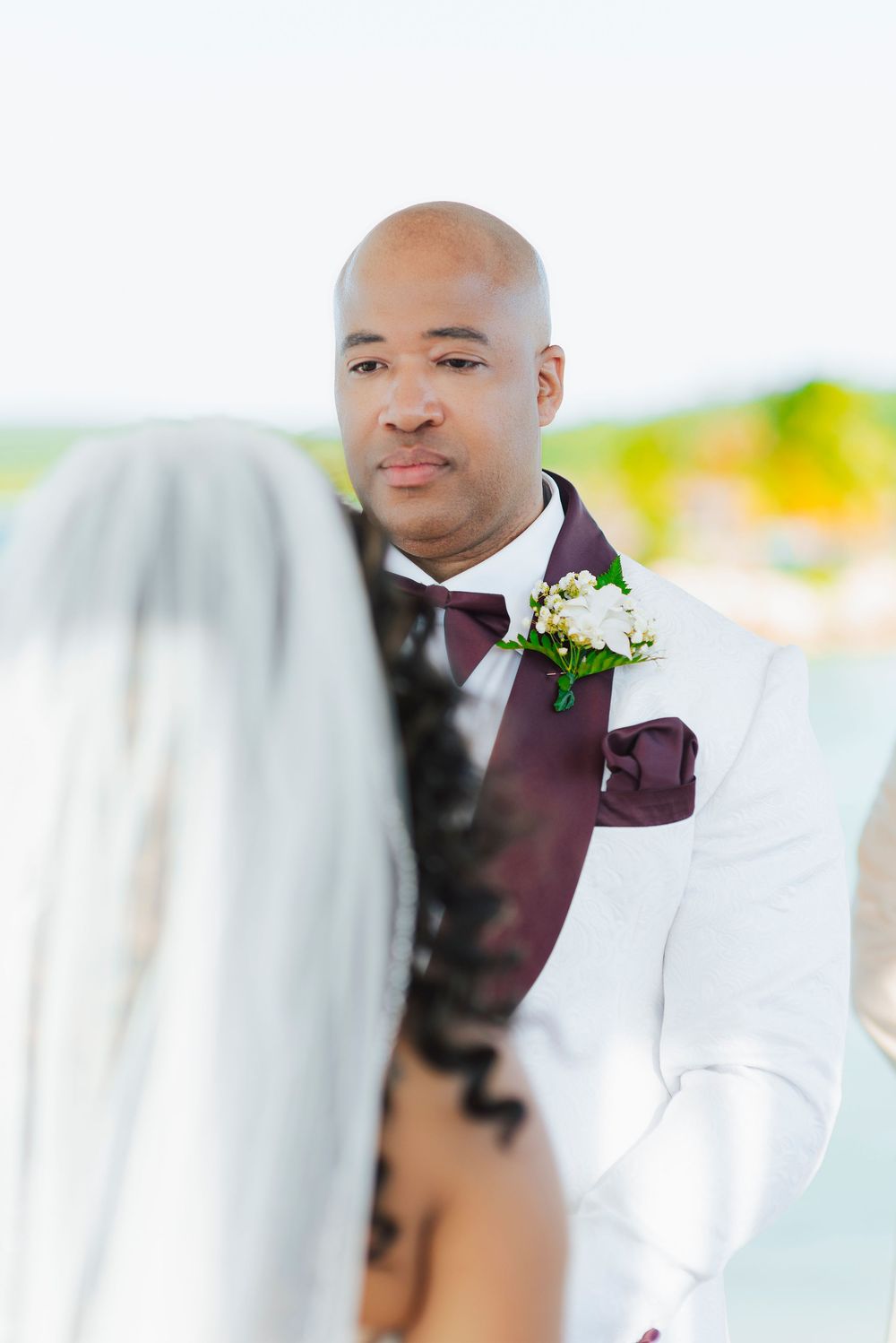 Close-up portrait shots of a groom in a white suit jacket and burgundy bow tie on a beach.