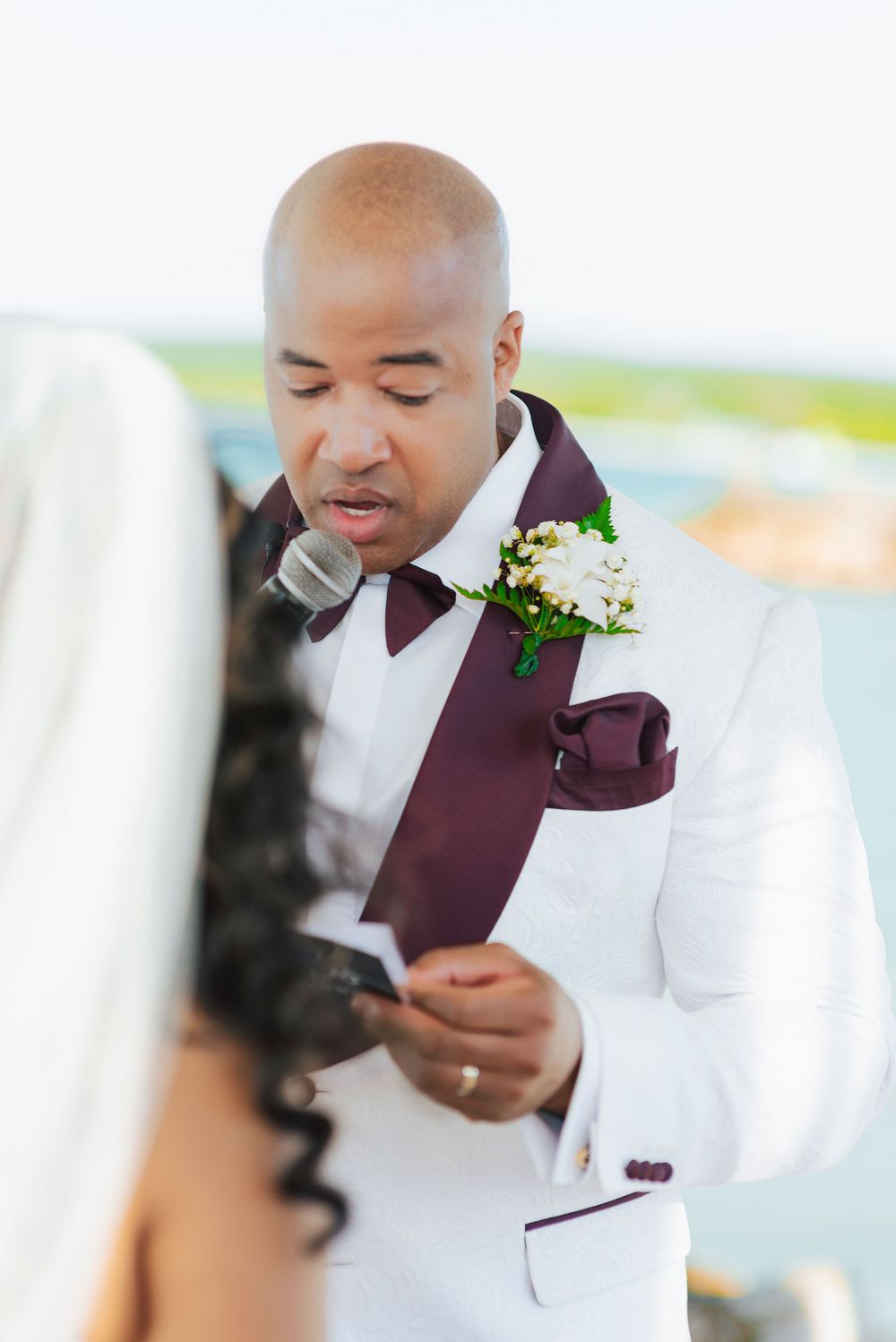 Groom in white suit with burgundy vest smiles and poses during wedding photoshoot.