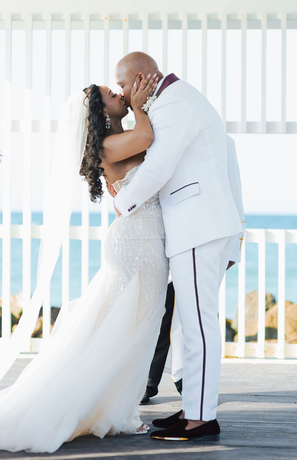 Wedding couple shares romantic dips and kisses on a white deck overlooking the ocean.