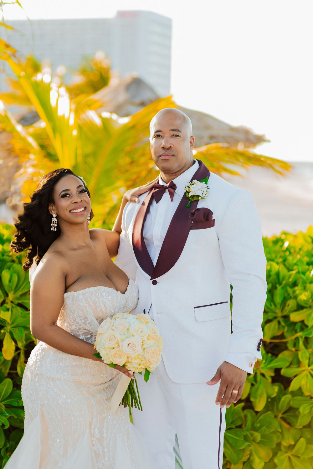A radiant couple poses for their wedding photo against vibrant yellow palm trees and greenery.