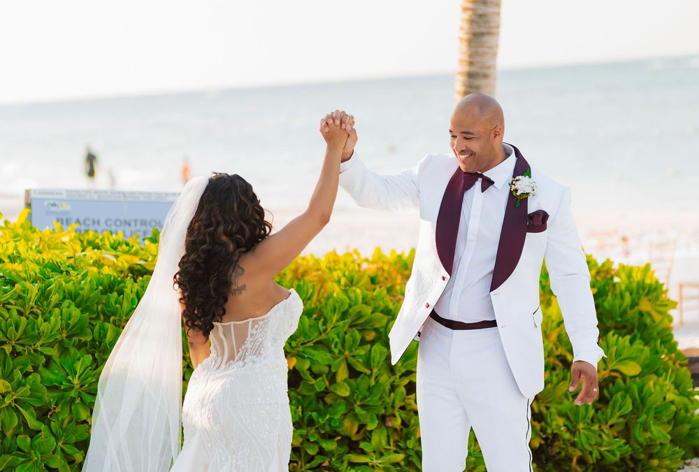 A romantic wedding couple poses on a tropical beach with palm trees and ocean views in the background.