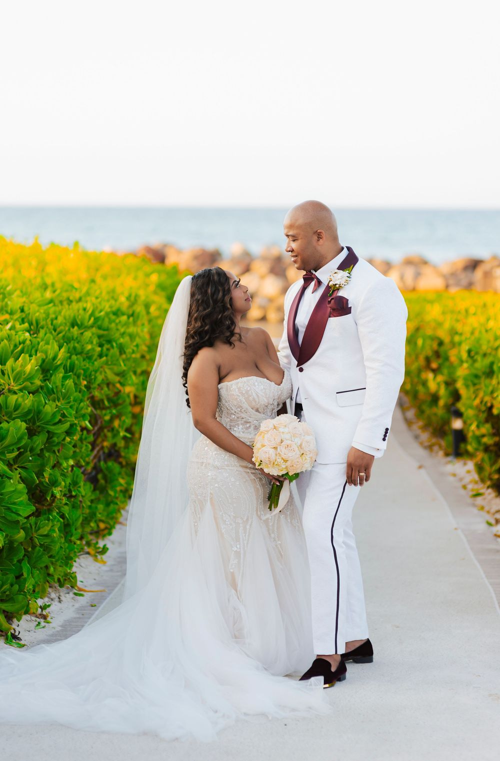Newlyweds pose together in a vibrant yellow flower field at their beach wedding.