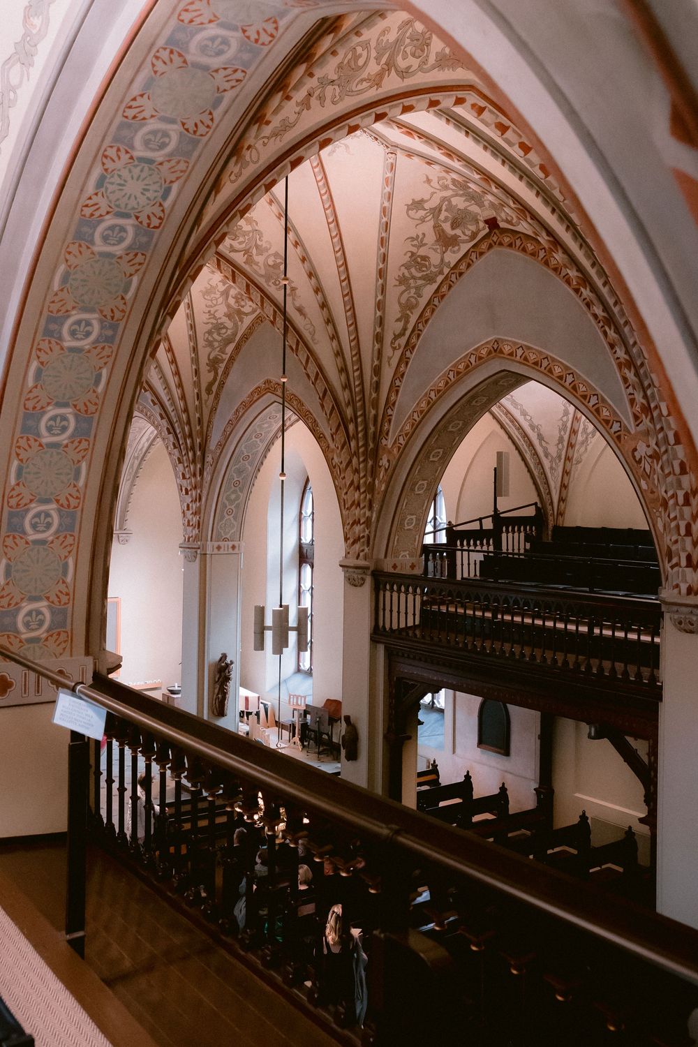 Ornate vaulted cathedral ceiling with decorative paint and wooden balcony in a church interior.