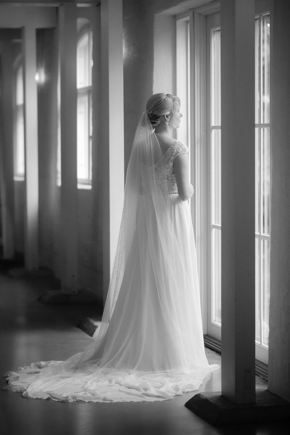 A series of romantic black and white photos showing a wedding dress and veil in a light-filled hallway.