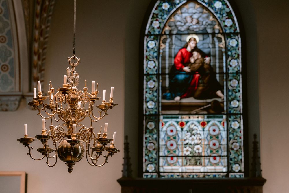 Beautiful stained glass window and ornate brass chandelier inside a historic church's sanctuary.