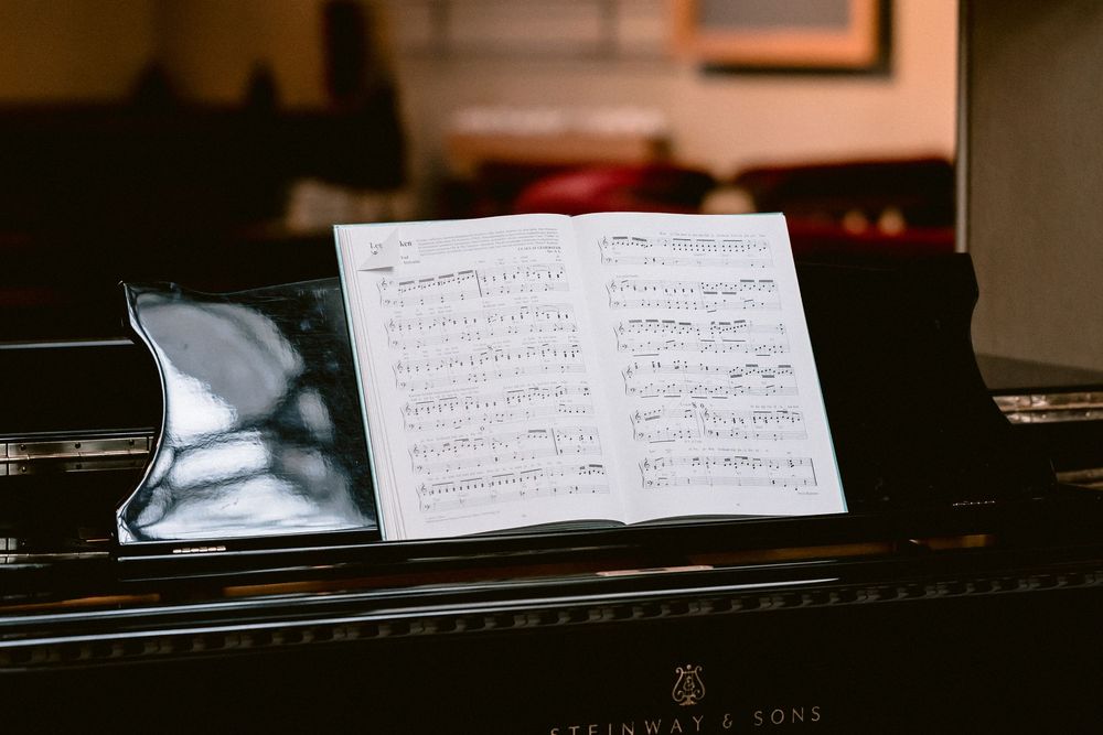 Sheet music rests on a black piano keyboard in a dimly lit room with warm lighting.