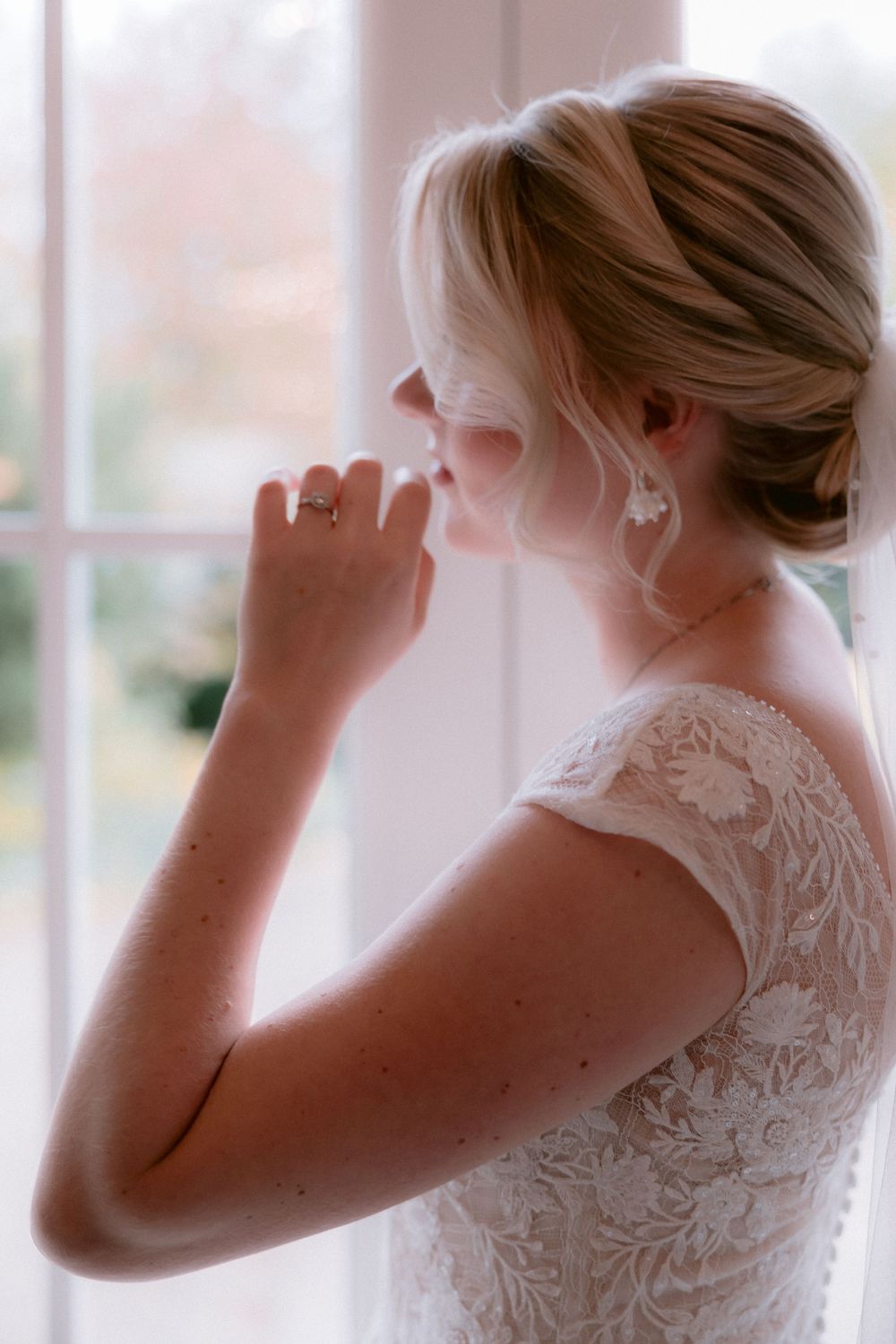 Artistic bridal portrait showing intricate lace back detail of wedding gown near window.