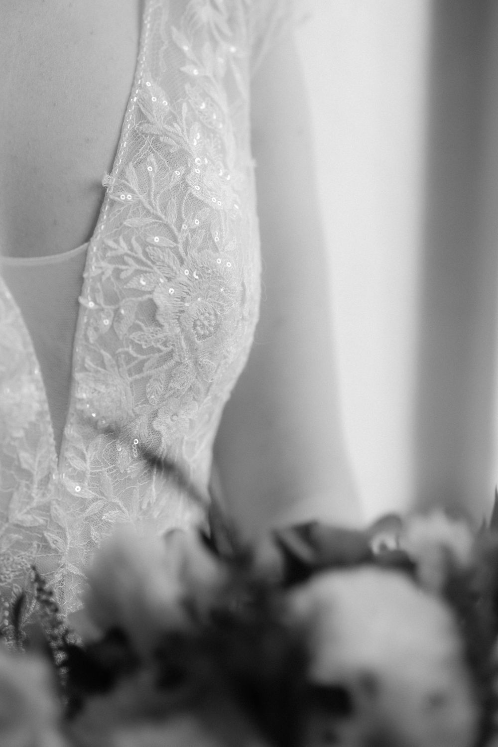 Close-up detail shot of delicate white lace wedding dress fabric with floral embroidery in black and white.