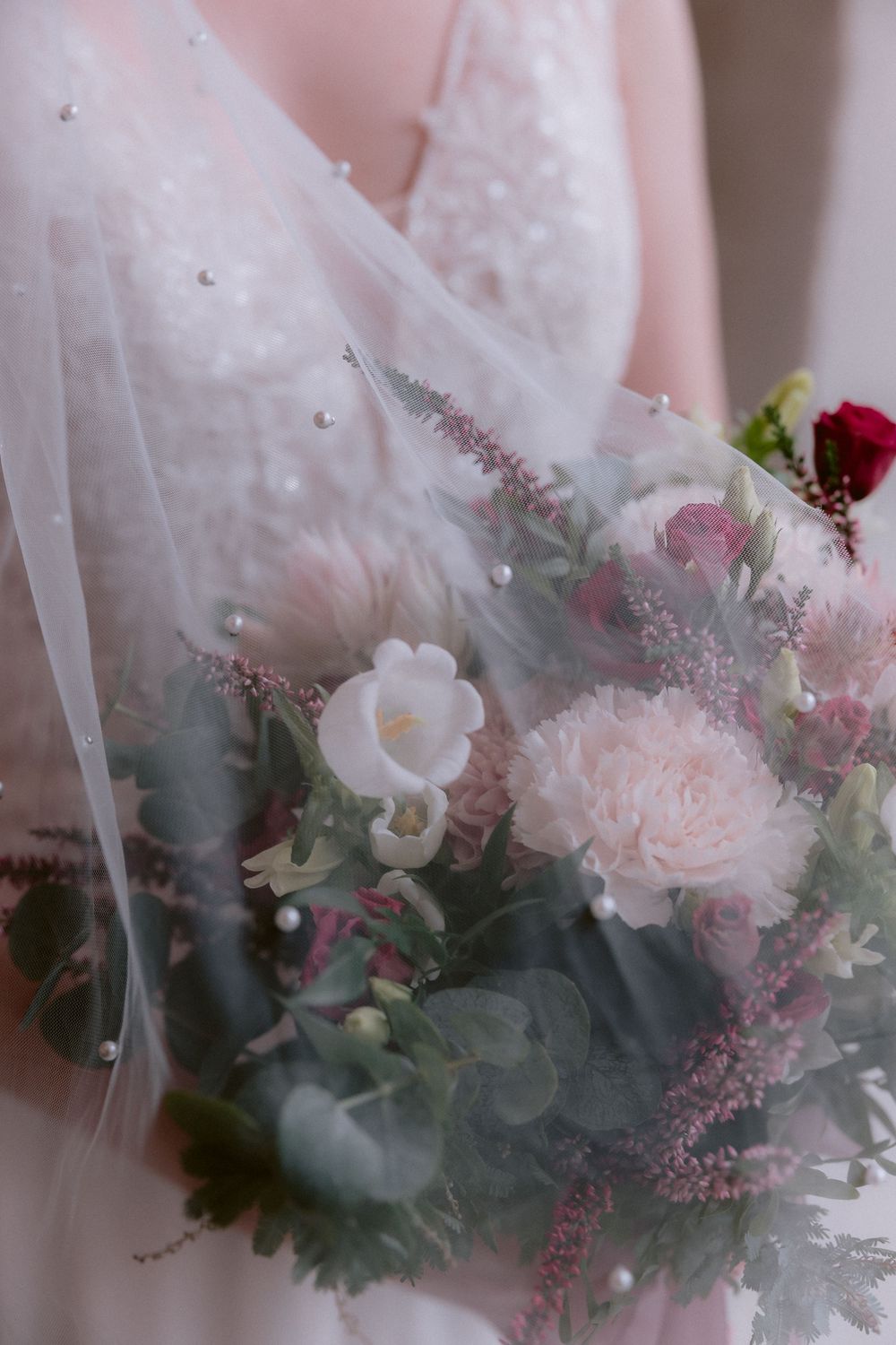 Dreamy floral arrangement with soft pink roses, white flowers, and dusty green foliage wrapped in delicate tulle fabric.