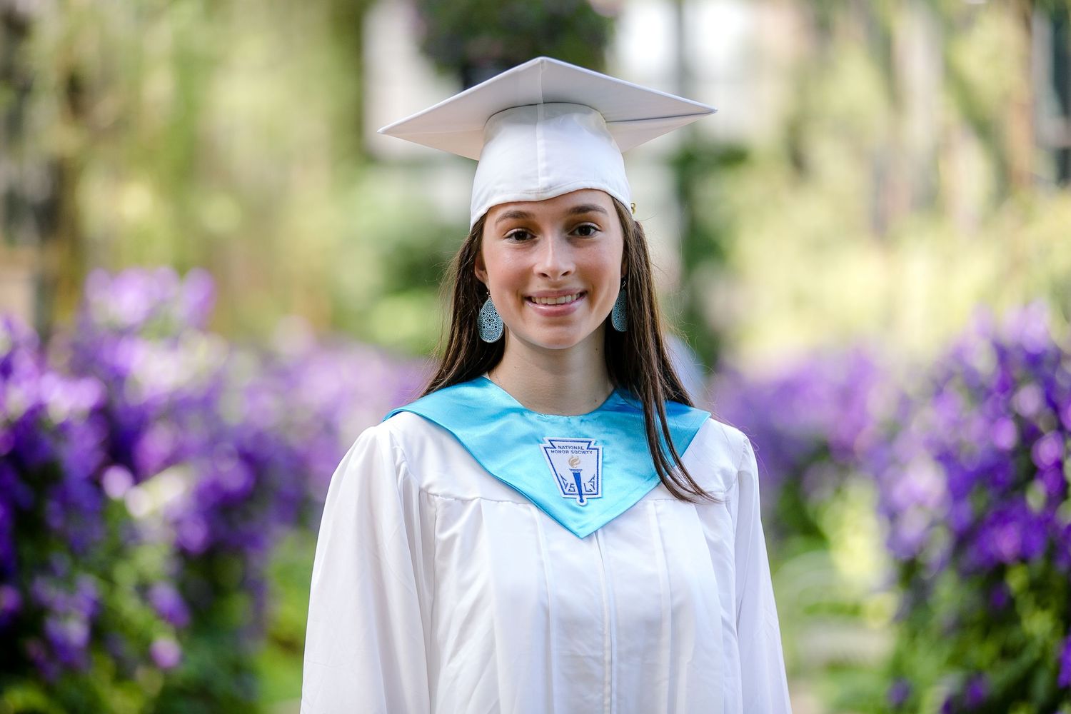 A composite of graduation photos showing someone in a white cap and gown against purple spring flowers and trees.