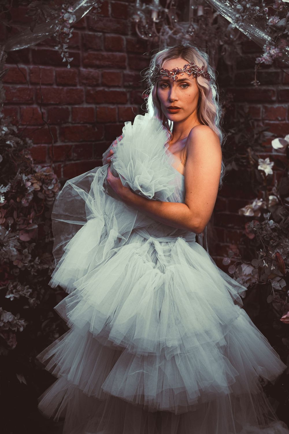 Ethereal bridal portrait featuring a layered tulle gown and delicate crown against a rustic brick wall backdrop.
