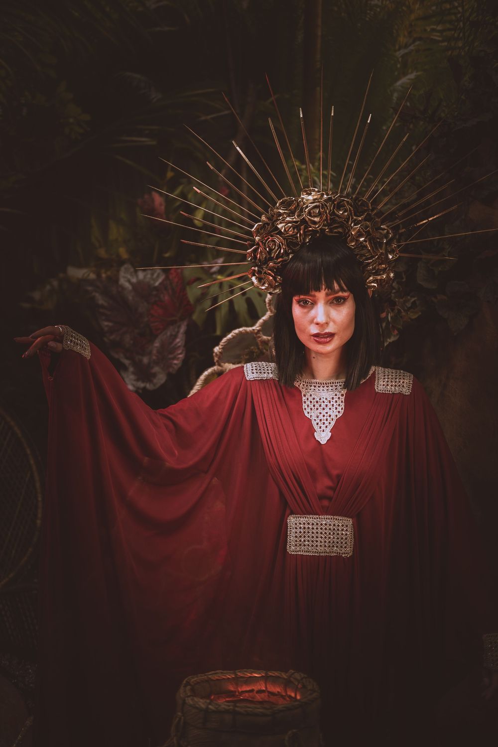 A dramatic fashion portrait featuring a red flowing cape and spiked crown headpiece against a dark background.