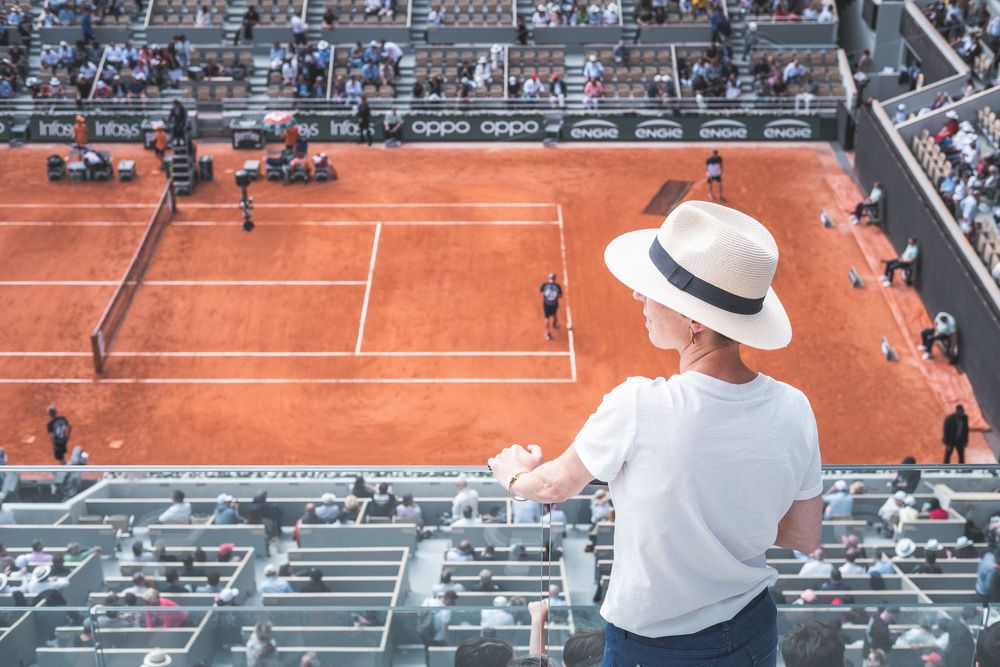 Aerial view of clay tennis court during tournament with spectators in stands.
