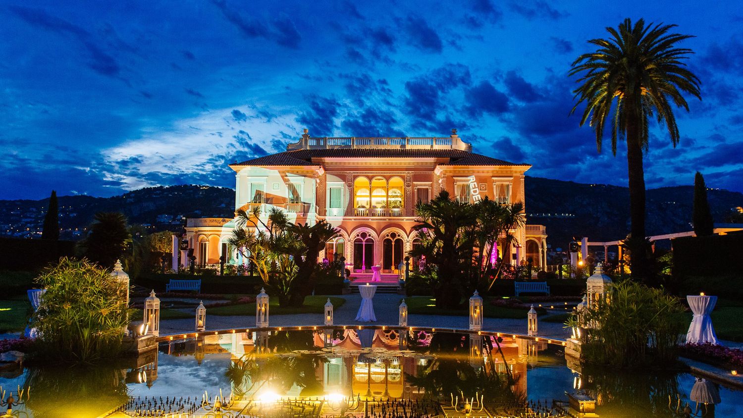 Panoramic view of an illuminated luxury venue with palm trees at dusk.