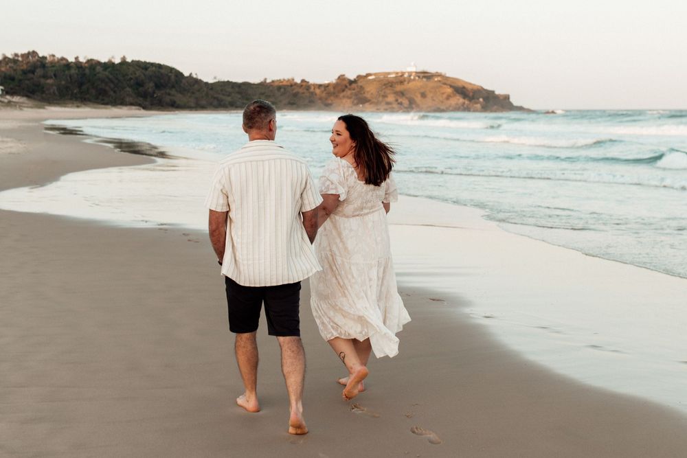 Couple walking along a beautiful sandy beach at sunset with waves crashing.