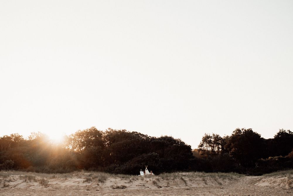 Panoramic view of a beach setting with decorative teepees and natural scenery at dusk.
