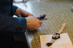 Hands work on a measuring task at a workbench with a ruler and tools against a textured surface.