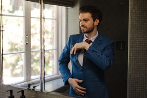 Professional wearing a navy blue button-down shirt leans against wall in modern office space.